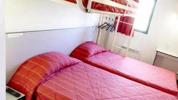 A bunk bed room with two beds, each with red bedding. There is a small table and a chair in the corner.