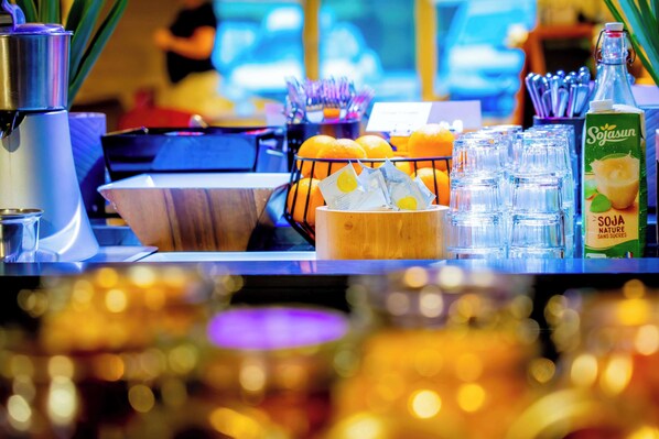 A bar area with a coffee machine, a bowl of oranges, a juice dispenser, and a bottle of Soya Suga.