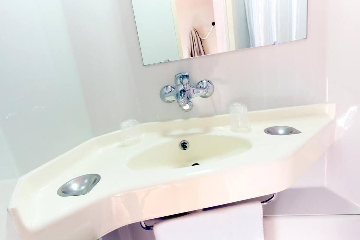 Un baño con un lavamanos blanco, un espejo encima y una toalla en un perchero.