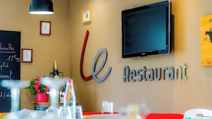Een restaurantinterieur met een krijtbordmenu, een aan de muur bevestigde televisie en een rode stoel op de voorgrond.