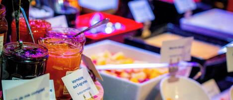 A buffet with various food items and drinks, including a bowl of fruit and a container of yogurt.