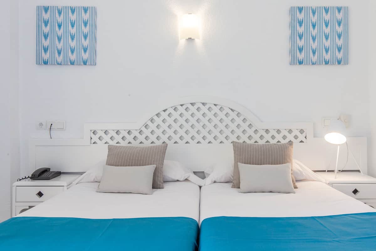 A double bed with a white headboard, two bedside tables with lamps, a phone, and a wall-mounted light fixture.