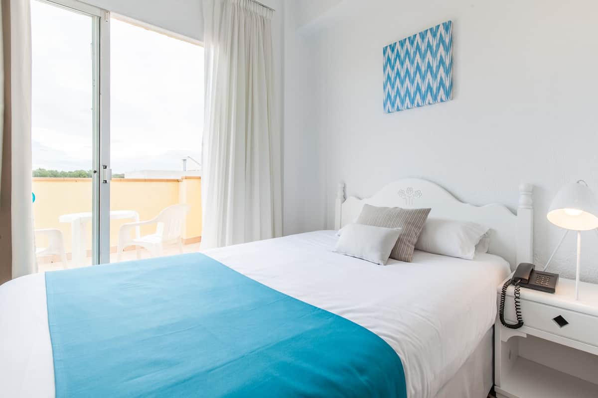 A hotel room with a bed, a nightstand, a lamp, a phone, and a view of the outside.