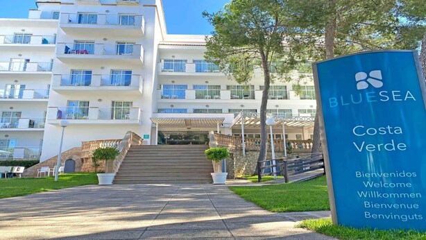 A BLUESEA Costa Verde hotel entrance with a staircase leading to the building, a signboard, and a clear sky. - BLUESEA Costa Verde (Llucmajor)