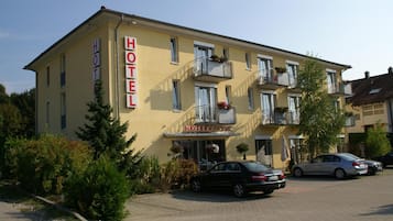 Un hotel de dos pisos con fachada amarilla, balcones con plantas en macetas y un letrero que dice "HOTEL CLASSIC".
