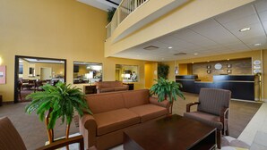 A hotel lobby with a brown sofa, a wooden coffee table, and striped chairs. There is a reception desk with a sign above it. - Comfort Inn & Suites adj to Akwesasne Mohawk Casino (Hogansburg)