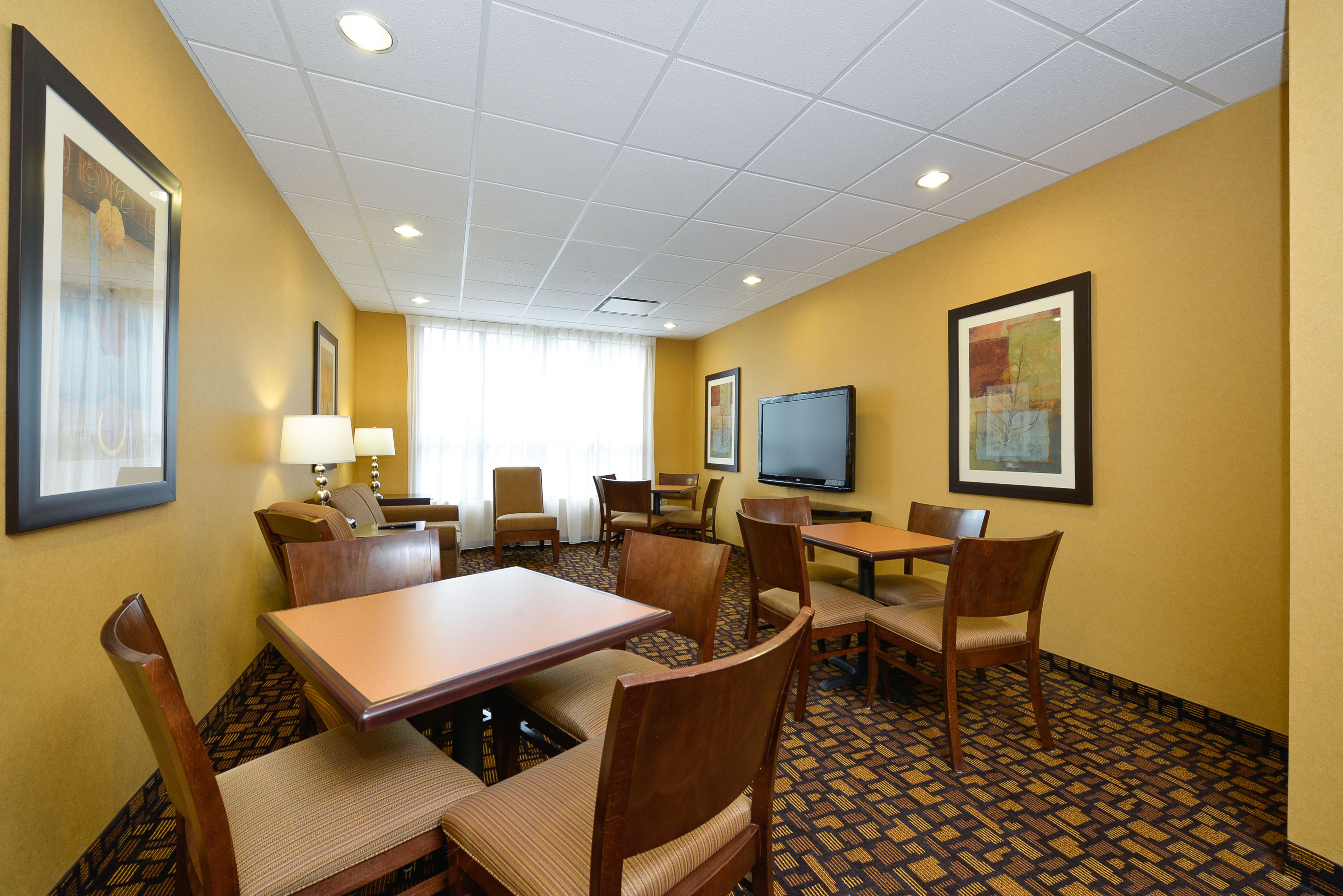 A hotel room with a dining area, a TV, and framed artwork on the walls.