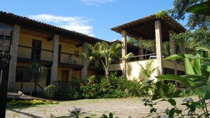 A courtyard with a building featuring a tiled roof, stone pillars, and a covered seating area. - Pousada Aguas de Paratii (Paraty)