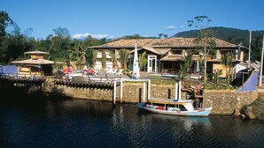 A waterfront property with a boat dock, a swimming pool, and a building with a tiled roof. - Pousada Aguas de Paratii (Paraty)