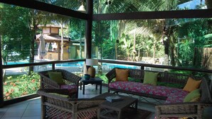 A sunlit room with wicker furniture, a pool view, and a tropical garden. - Pousada Aguas de Paratii (Paraty)