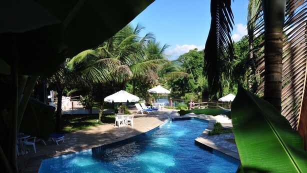 A swimming pool with lounge chairs and umbrellas, surrounded by palm trees and greenery. - Pousada Aguas de Paratii (Paraty)