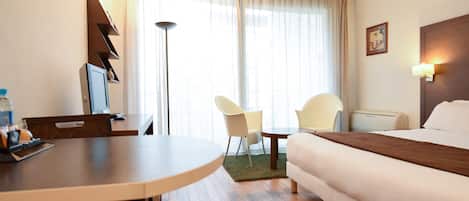A hotel room with a bed, a desk with a computer, a chair, and a lamp.