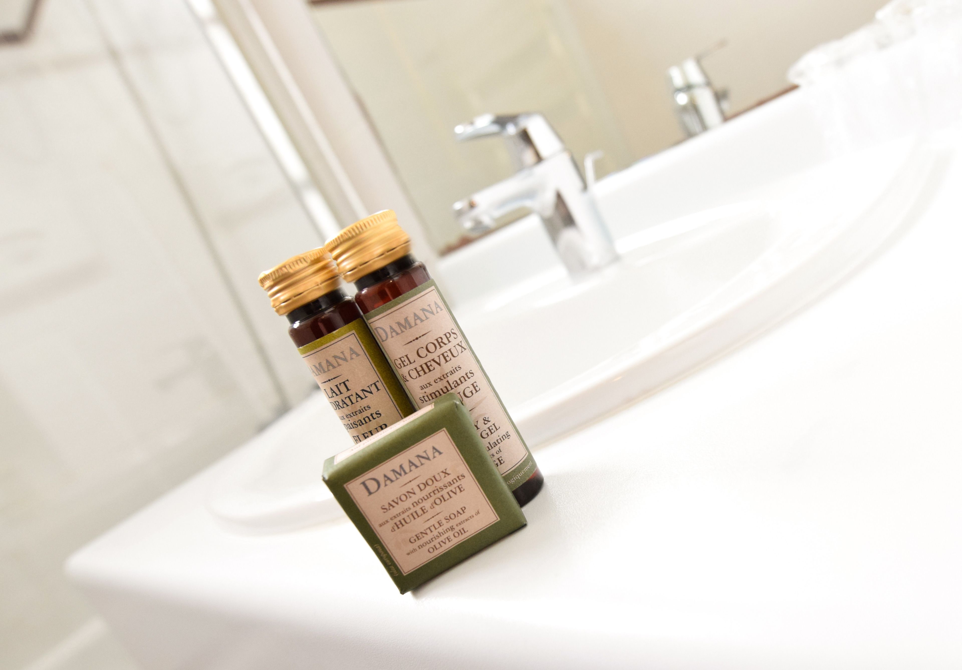 A bathroom with a white sink and two bottles of Damana soap on the counter.