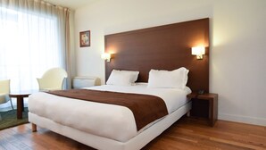 Una camera d'albergo con un letto grande, abat-jour, un tavolino e una sedia.