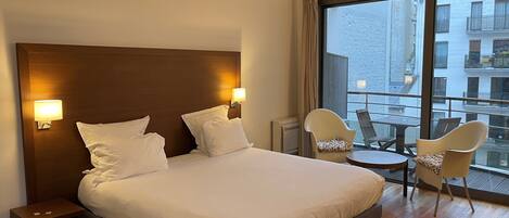 Une chambre d’hôtel avec un grand lit, deux lampes de chevet, une petite table et un balcon avec des chaises.