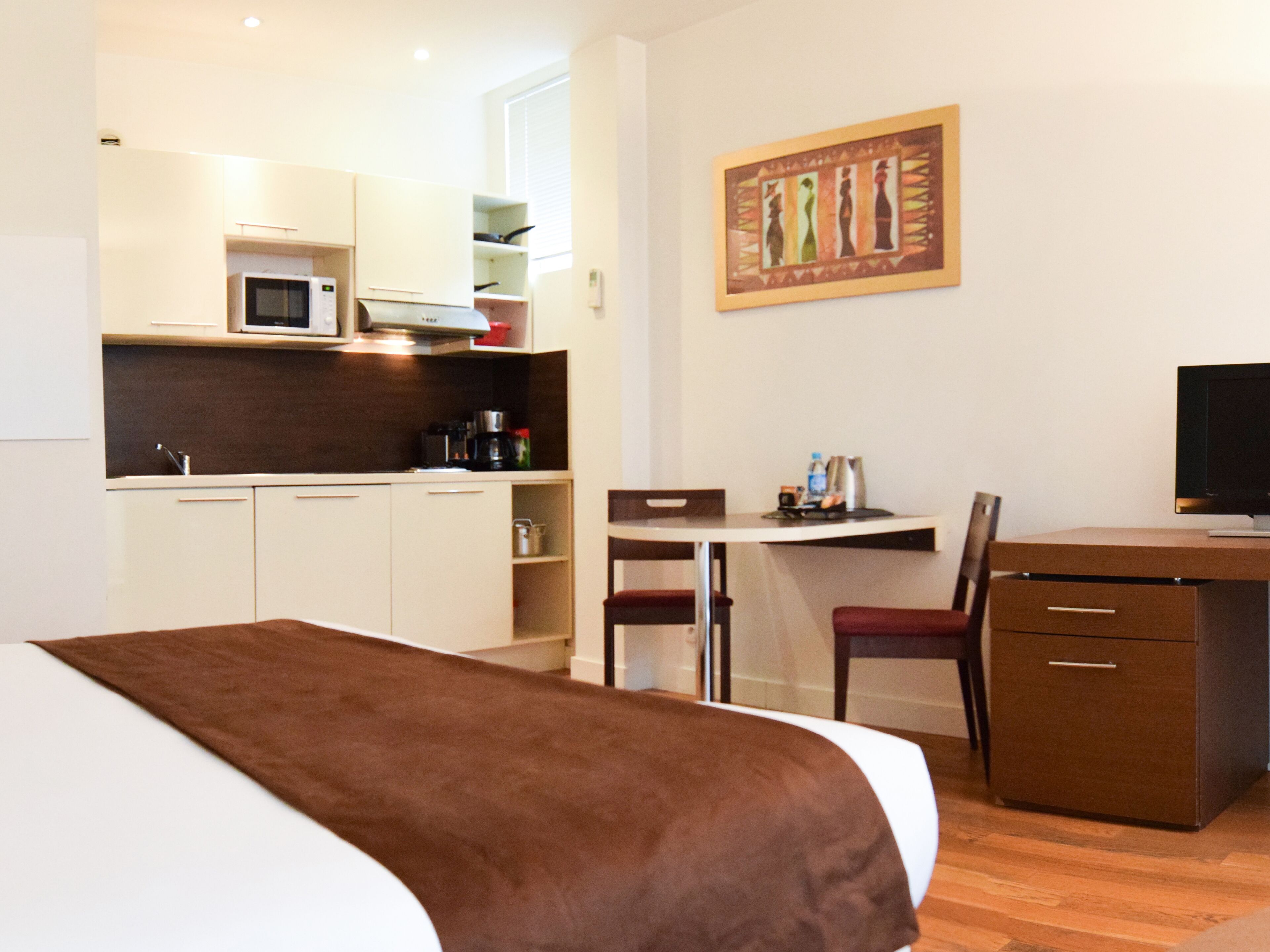 Een hotelkamer met een bed, een bureau, een stoel, een televisie en een kitchenette.