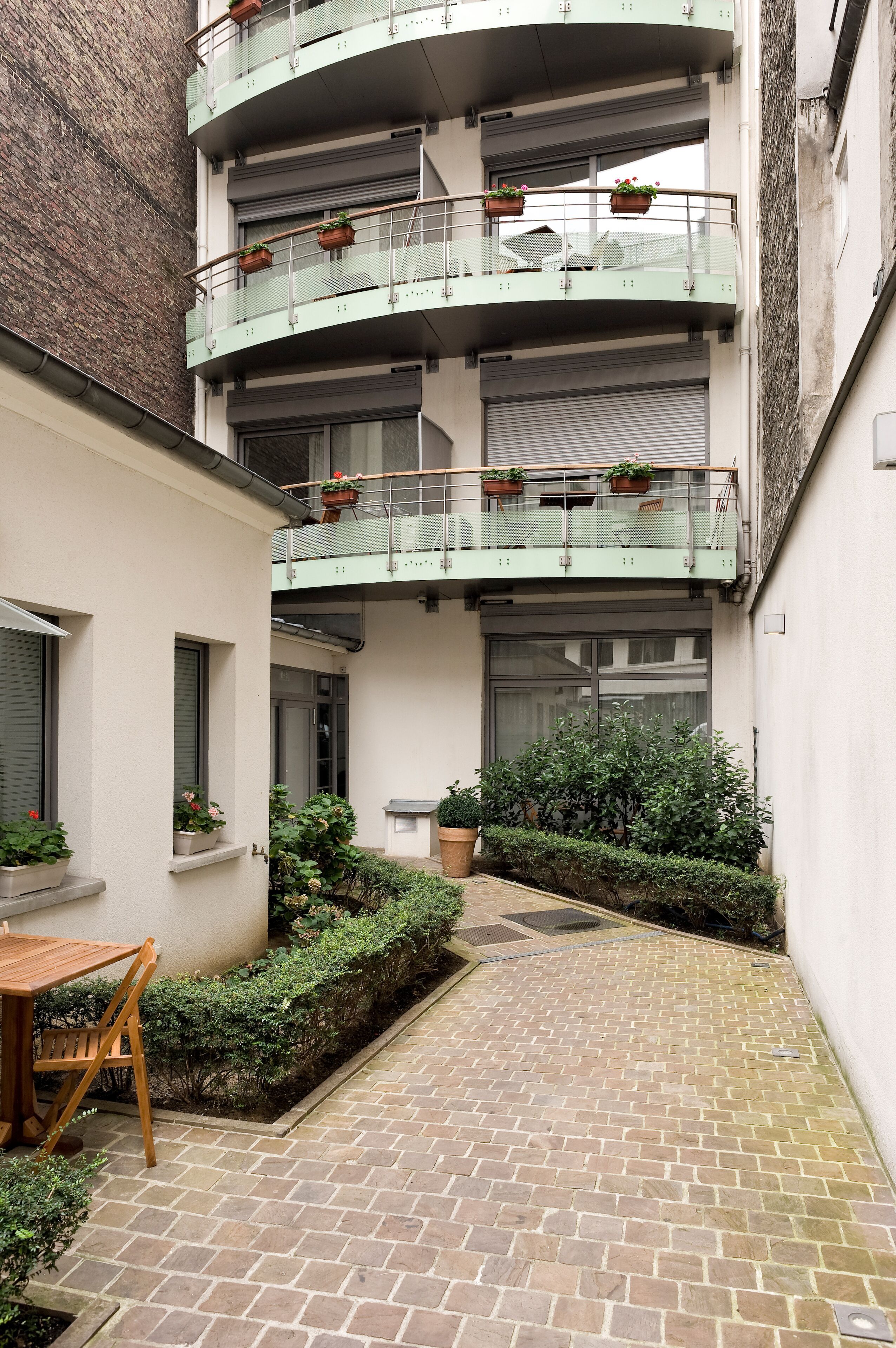 A multi-story building with balconies, potted plants, and a brick pathway.
