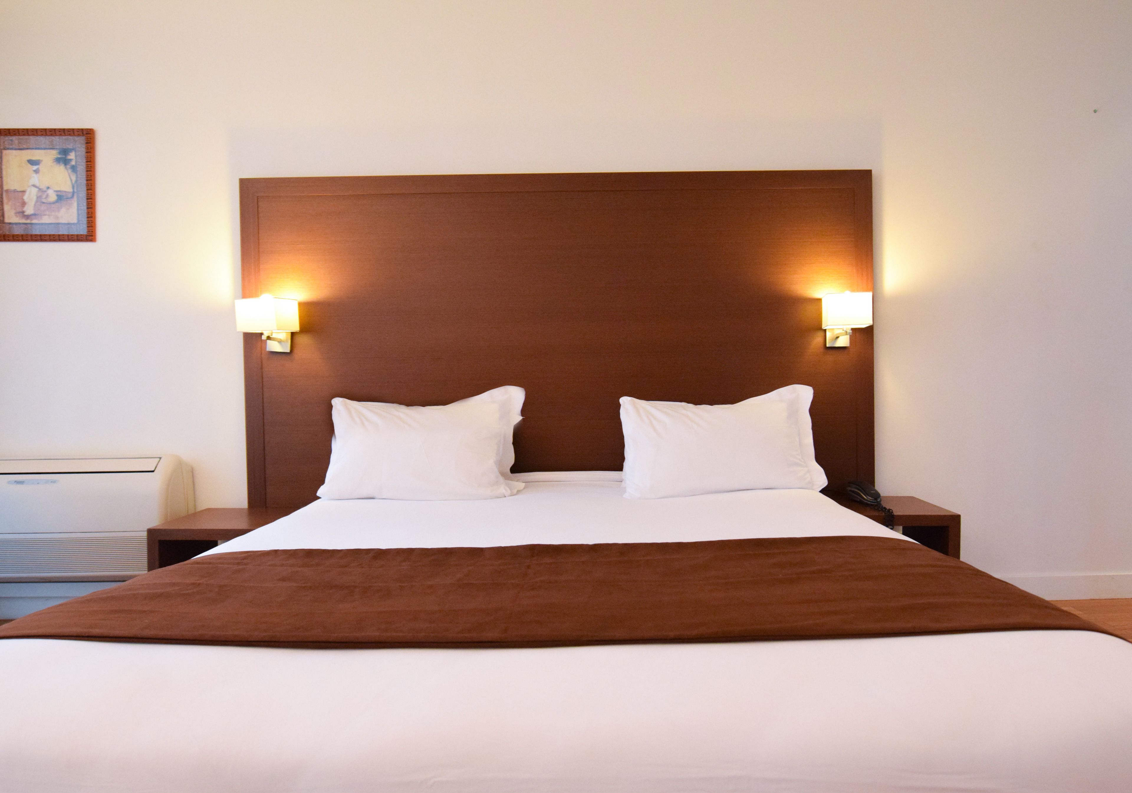 A hotel room with a large bed, two bedside lamps, and a nightstand with a phone.