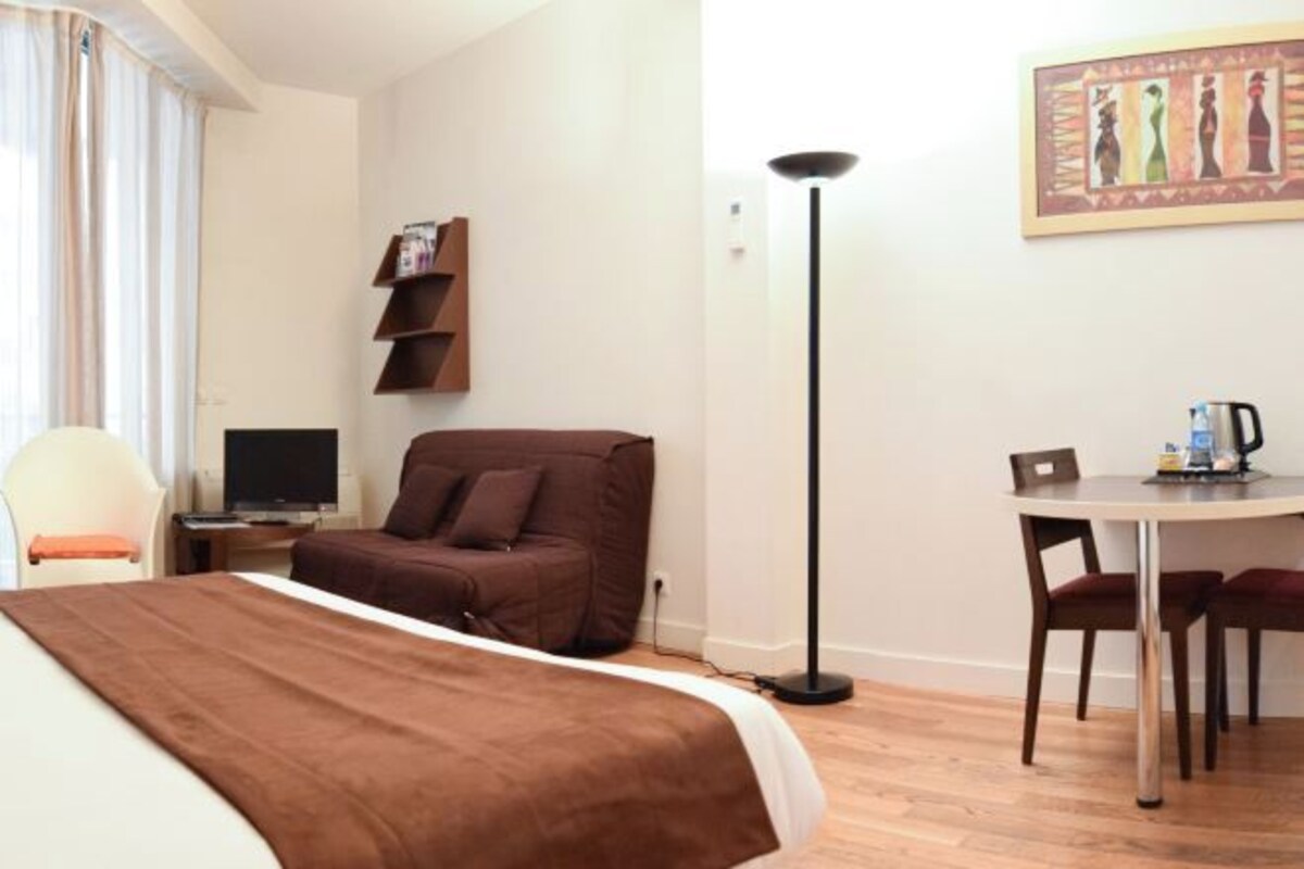 Una habitación de hotel con una cama, un escritorio, una silla, una mesa, una lámpara y un cuadro en la pared.