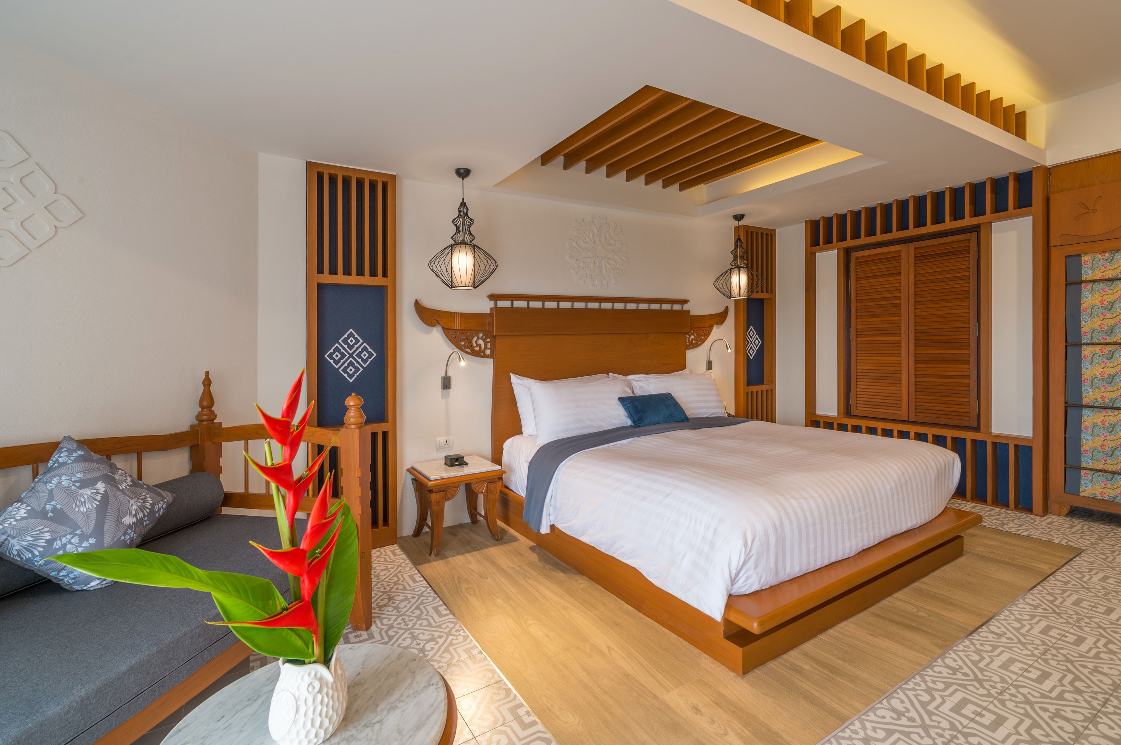 A bedroom with a large bed, wooden headboard, bedside lamps, a nightstand, a decorative plant, and a patterned rug.