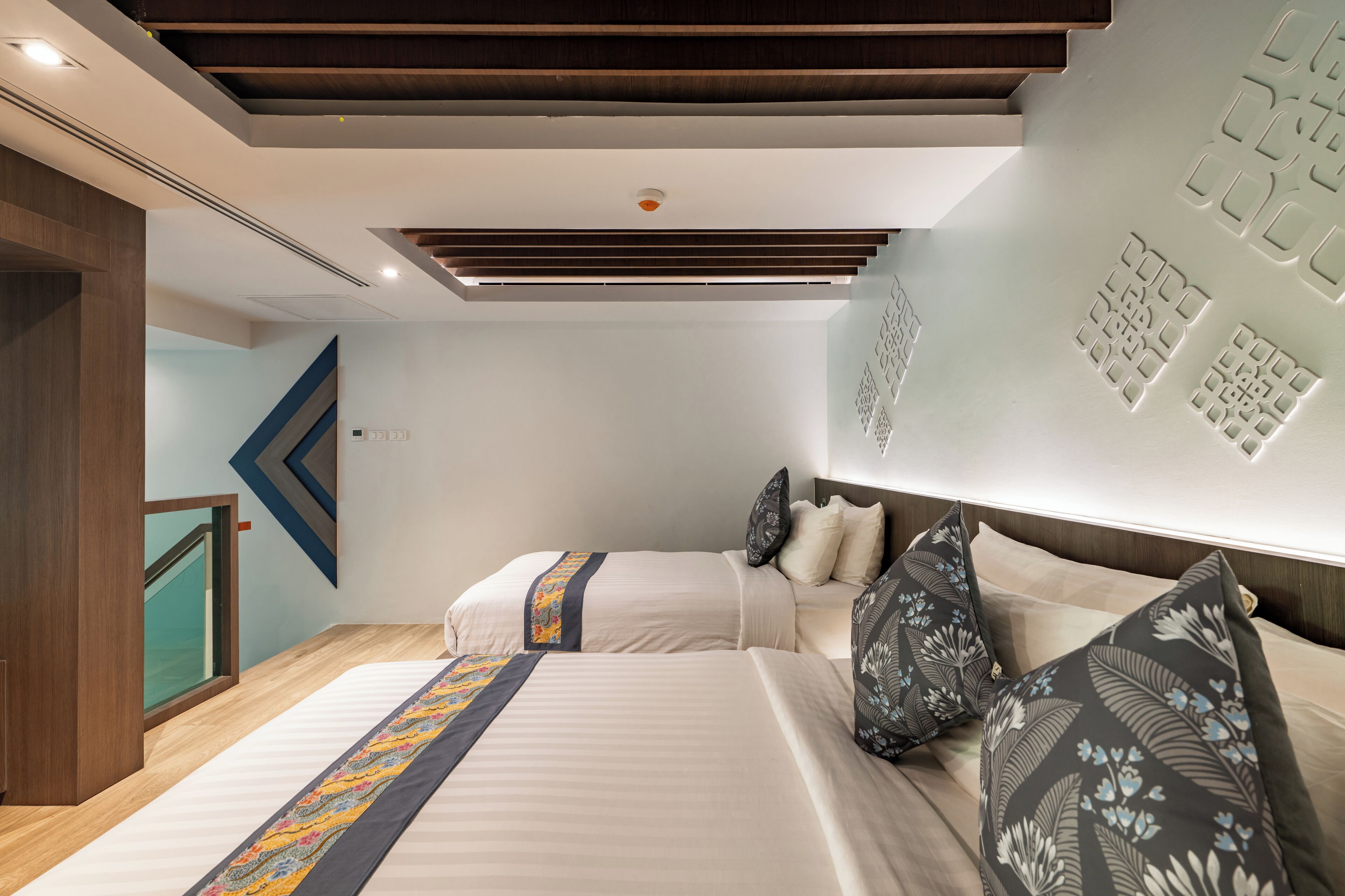 A modern hotel room with two beds, a wooden ceiling, and a geometric wall design.