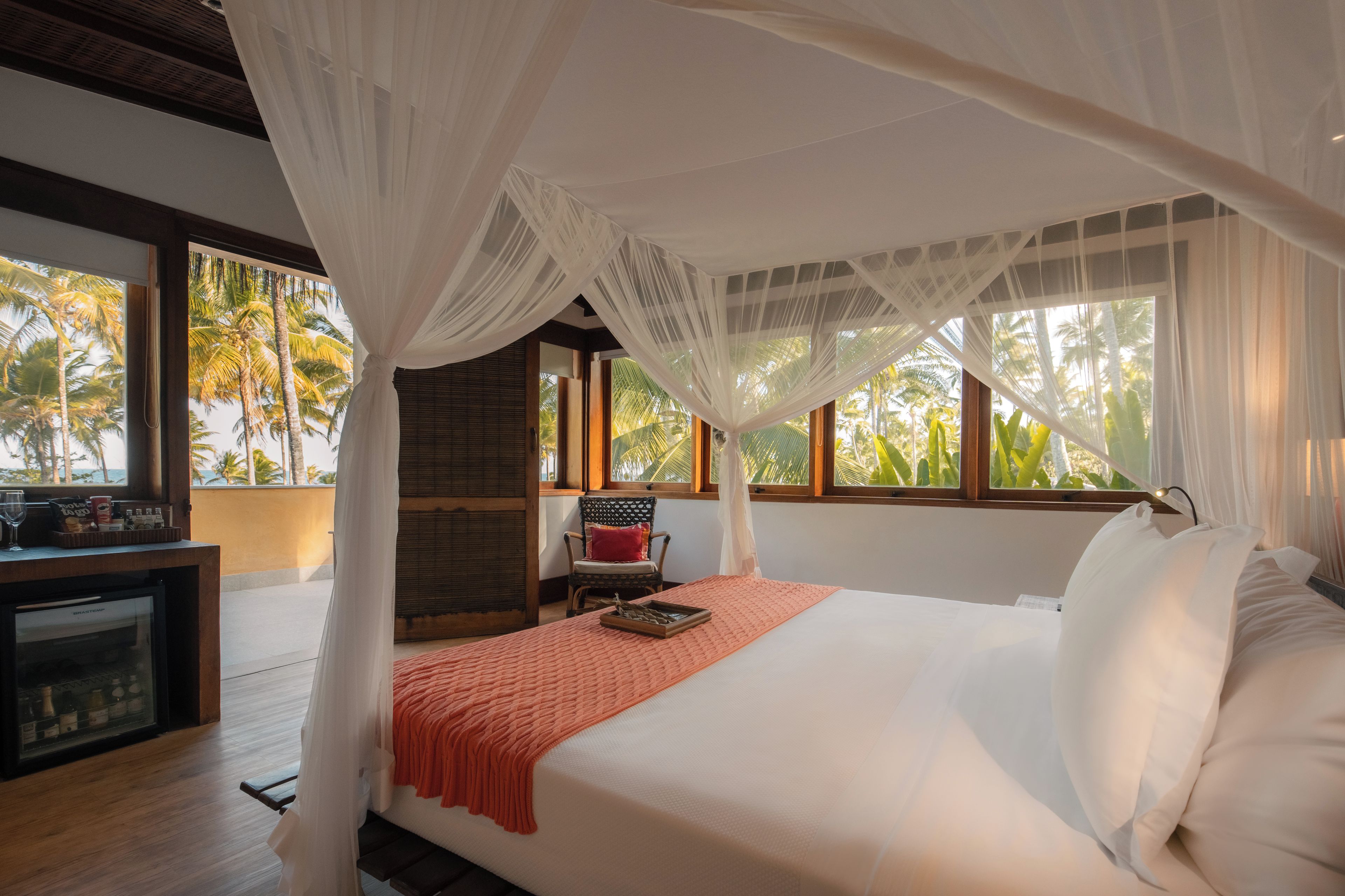 A bedroom with a canopy bed, a desk with a refrigerator, and a chair.