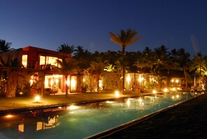 Ein Nachtblick auf einen Resort mit Schwimmbecken, Palmen und beleuchteten Gebäuden.