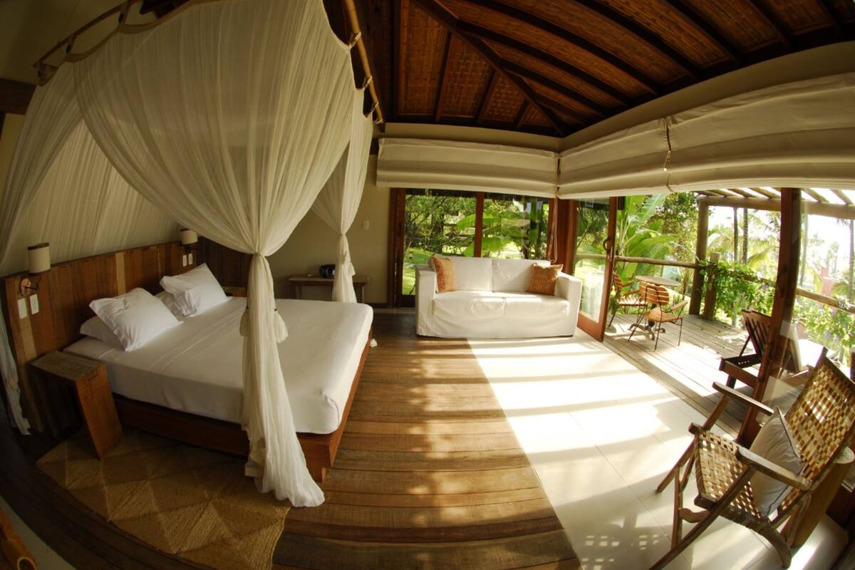 A room with a bed, a sofa, and a chair. There is a window with a view of greenery outside.