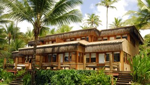 A two-story building with a thatched roof, surrounded by lush greenery and palm trees. - Txai Resort Itacaré (Itacaré)