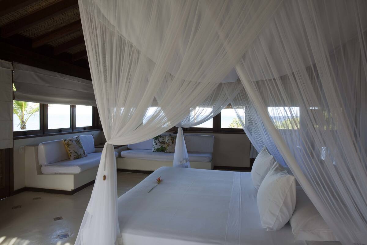 A bedroom with a canopy bed, a sofa, and a view of the outdoors.
