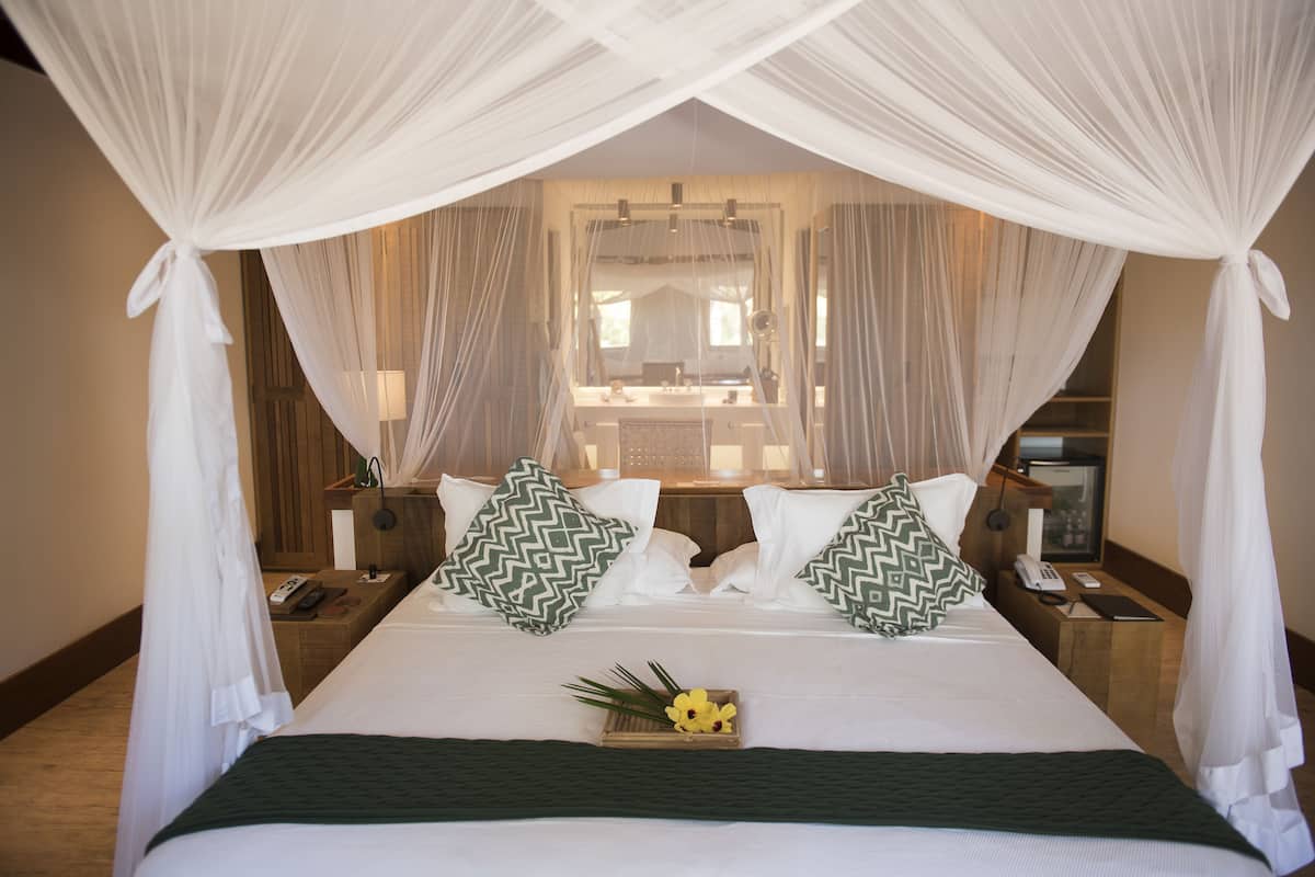 A hotel room with a large bed, white curtains, and a mirror above the bed.