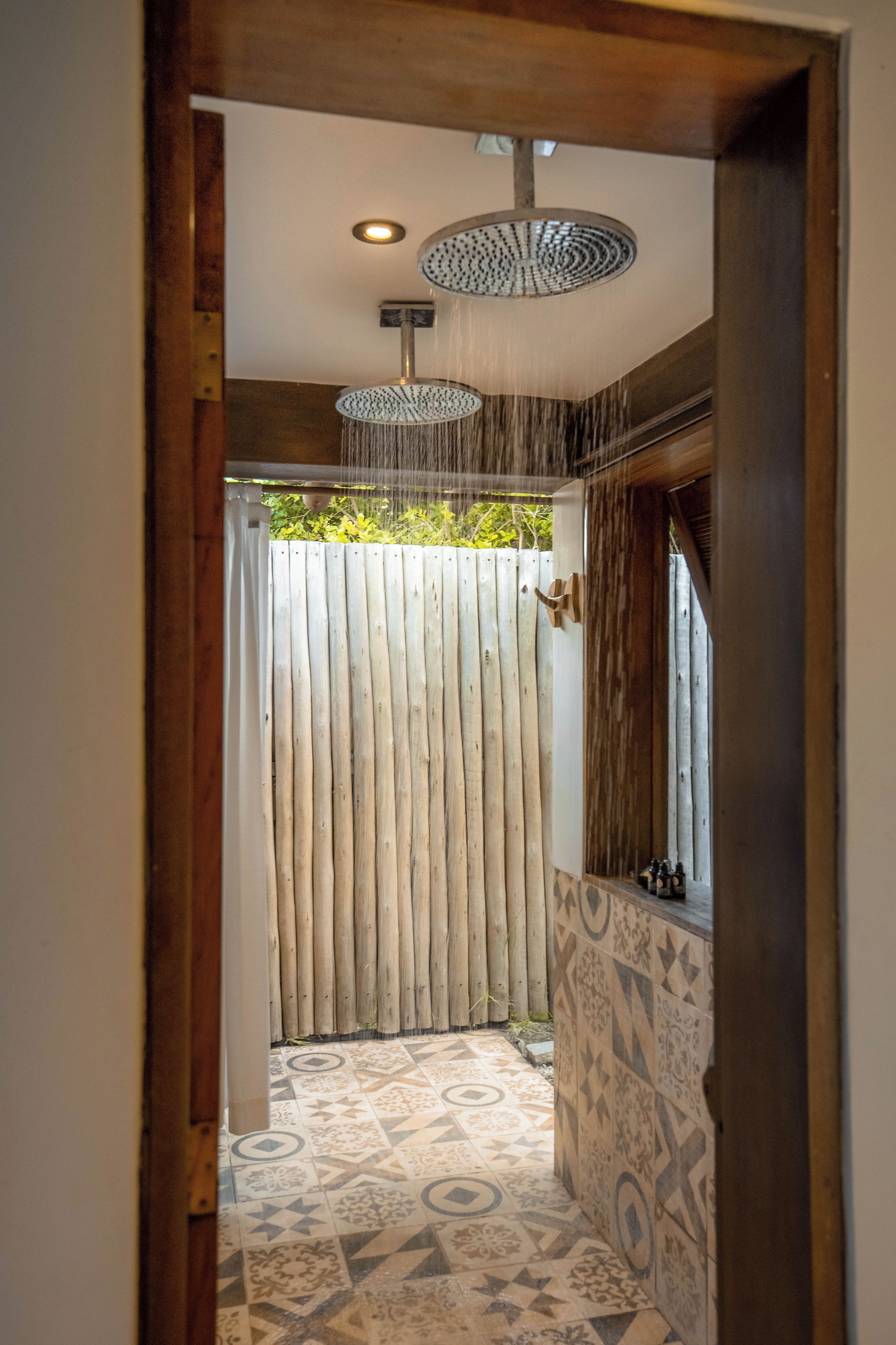 A shower area with a rain showerhead, a wooden fence, and patterned floor tiles.