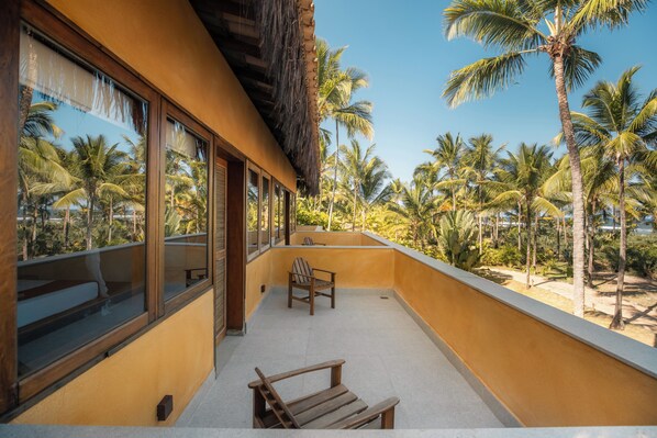Un balcón con una silla y un banco de madera, con vista a una playa con palmeras.