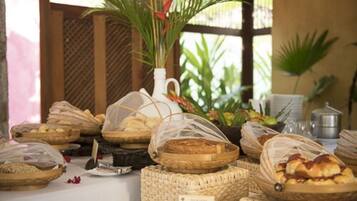 Uma mesa de buffet com diversos produtos de panificação em cestas, um jarro branco e uma pequena placa.