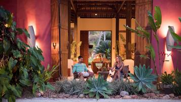 Una pareja sentada en muebles de exterior en un jardín tropical con una pérgola de madera.