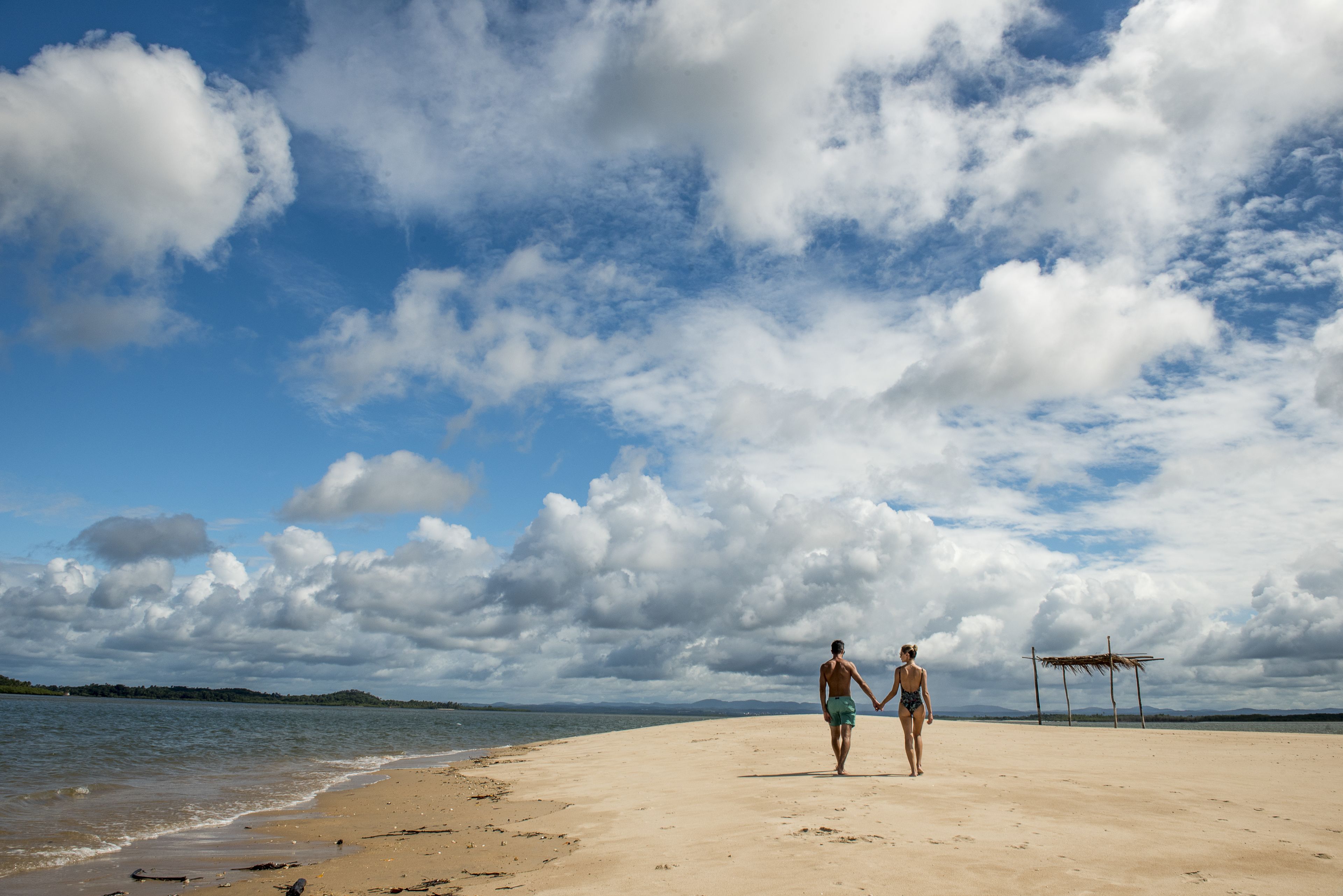A beach with a couple walking on the sand, a wooden structure, and a clear sky with clouds.