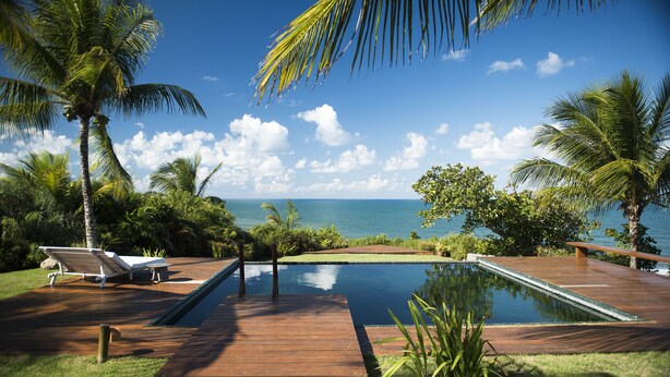 A wooden deck with a swimming pool, palm trees, and a view of the ocean. - Txai Resort Itacaré (Itacaré)