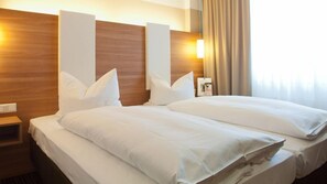 A hotel room with a large bed, wooden headboard, and a nightstand with a lamp. - Hotel Central (Neu-Isenburg)