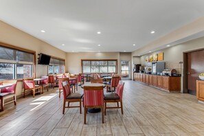 A spacious indoor area with multiple dining tables and chairs, a kitchen area with appliances, and large windows providing natural light. - Comfort Suites Huntsville MidCity District at Research Park (Huntsville)