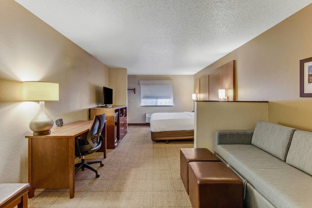 Une chambre d’hôtel avec un bureau en bois, une chaise, un lit, un canapé et un téléviseur.