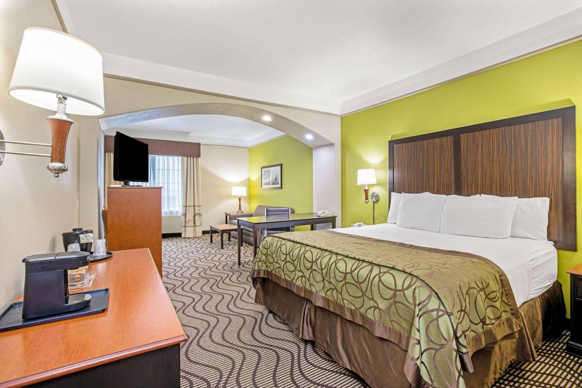 A hotel room with a bed, desk, and chair, a coffee machine, and a television.