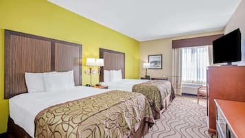 A hotel room with two beds, a television, a desk, and a window with curtains.