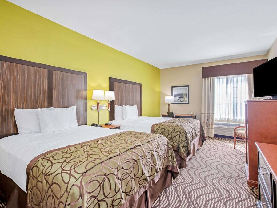 A hotel room with two beds, a television, a desk, and a window with curtains.