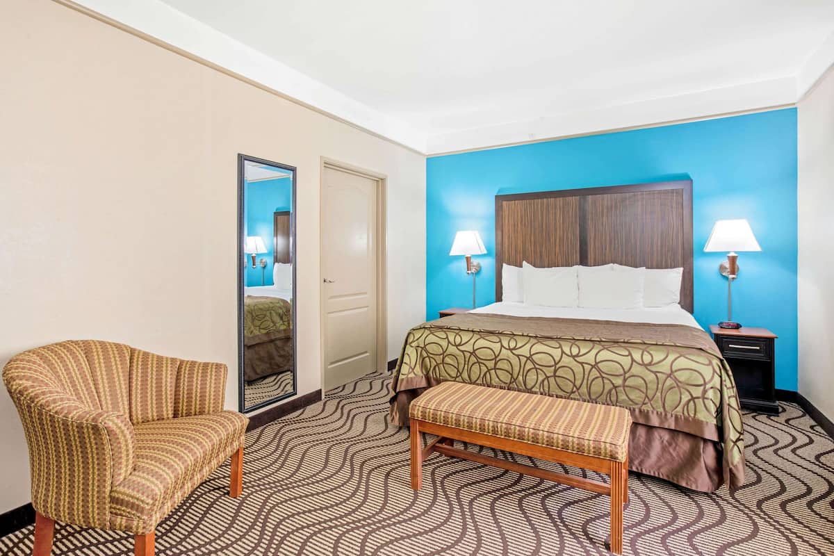 A hotel room with a bed, two bedside lamps, a chair, a bench, and a mirror.