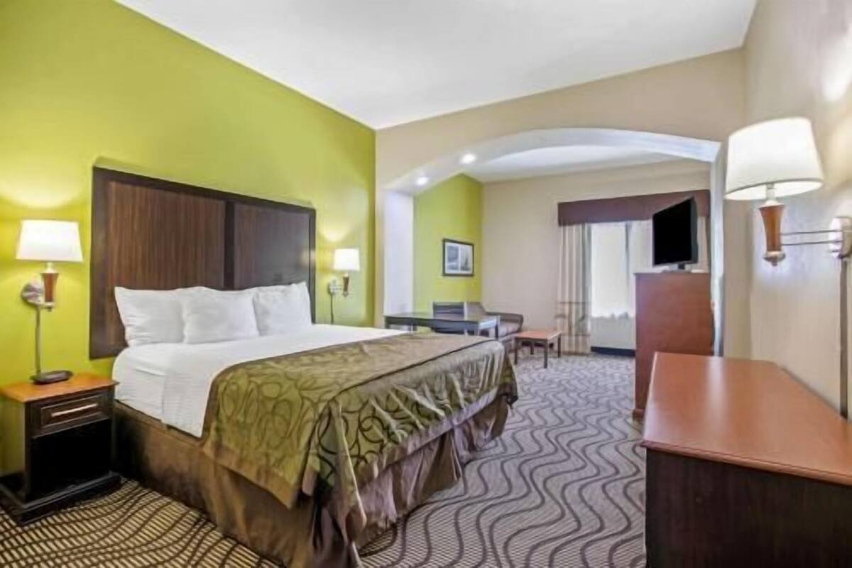 A hotel room with a bed, bedside tables, a desk, a chair, and a television.