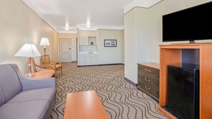 A hotel room with a sofa, a TV, a fireplace, a dining table, and a kitchen area in the background. - La Quinta Inn & Suites by Wyndham Corpus Christi Airport (Corpus Christi)
