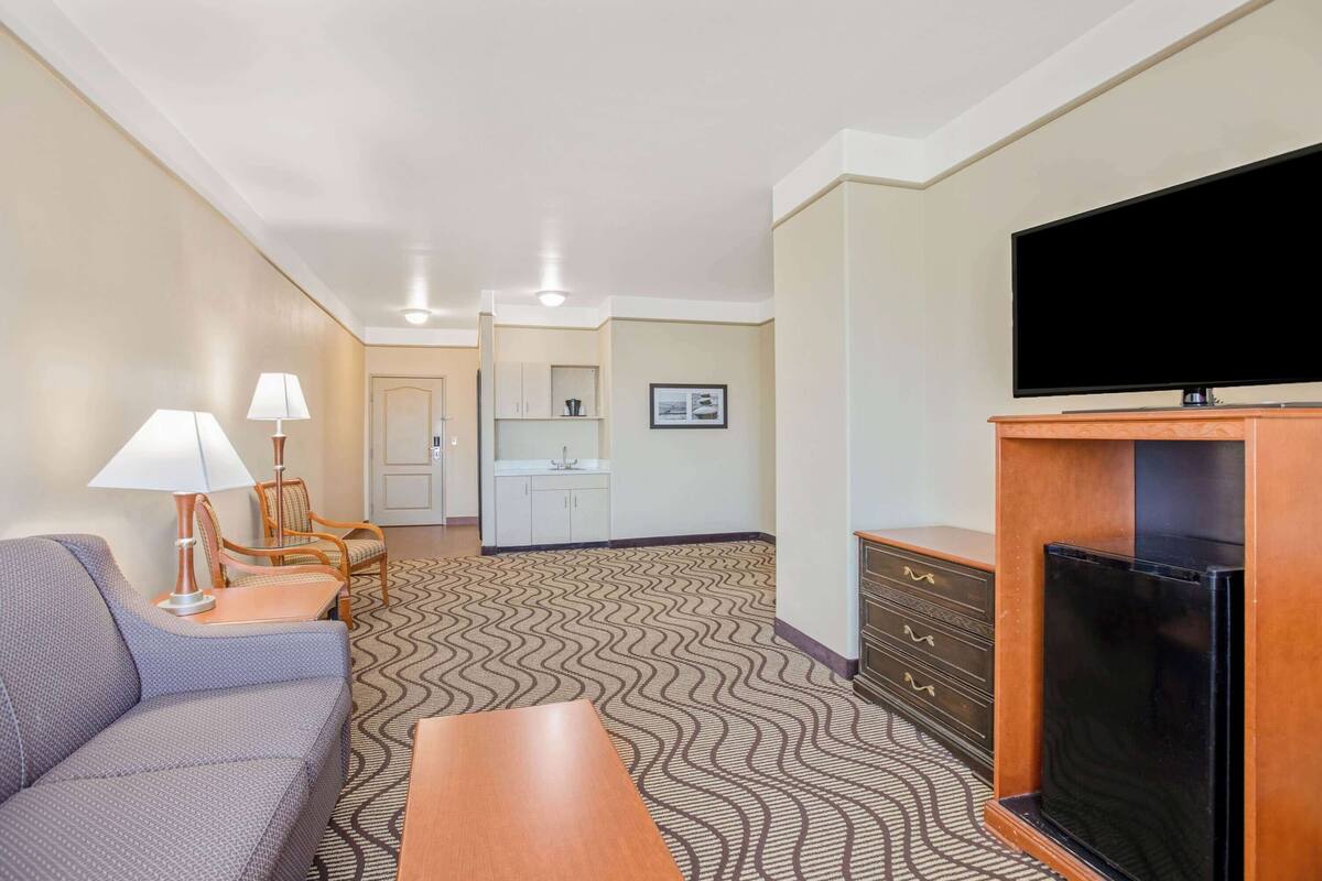 A hotel room with a sofa, a TV, a fireplace, a dining table, and a kitchen area in the background.