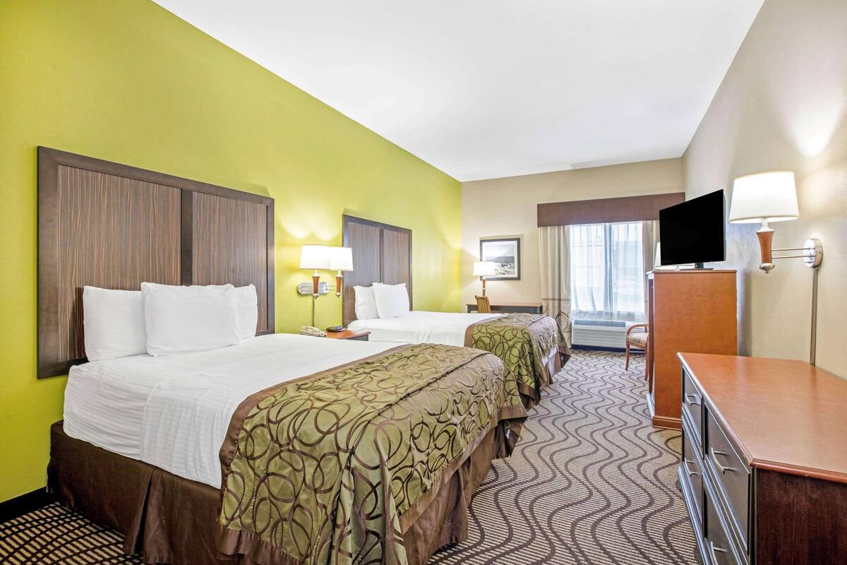 A hotel room with two beds, a desk, a television, and a window with curtains.