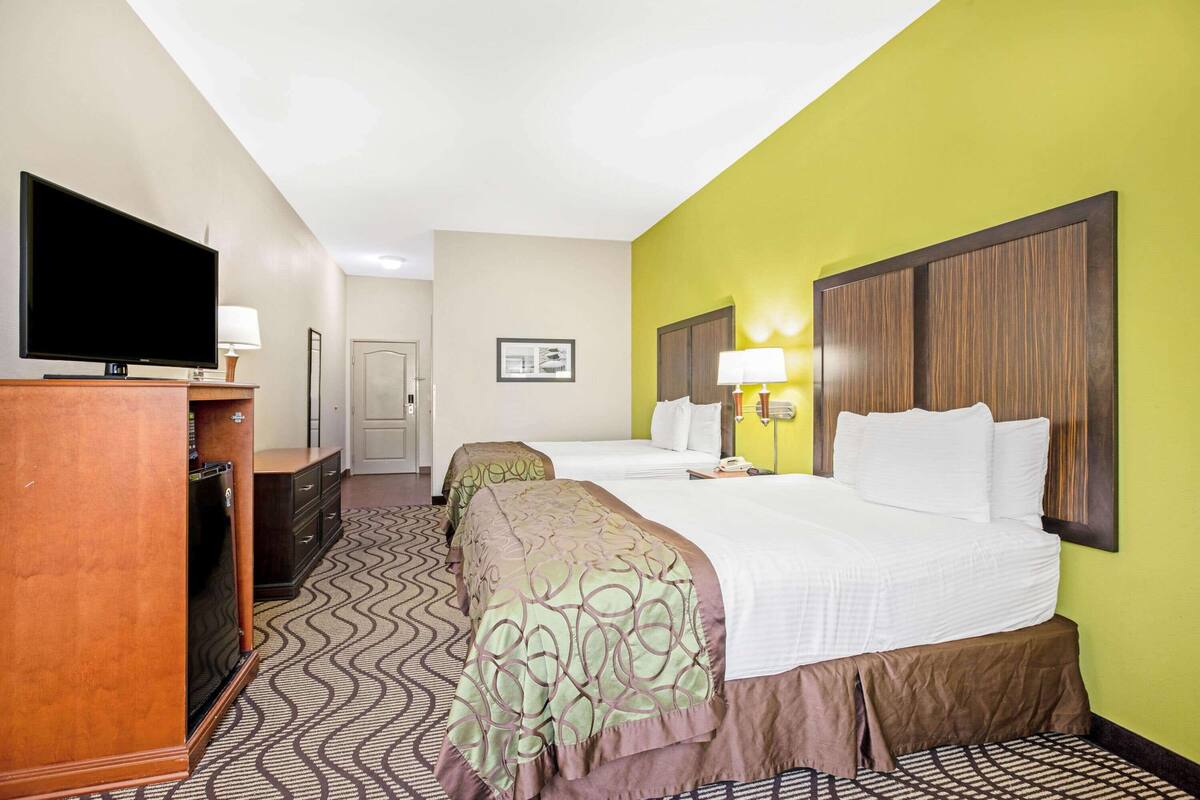A hotel room with two beds, a television, a desk, and a patterned carpet.