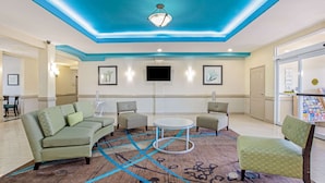 A lobby with a green sofa, two armchairs, a coffee table, and a patterned rug. - La Quinta Inn & Suites by Wyndham Corpus Christi Airport (Corpus Christi)